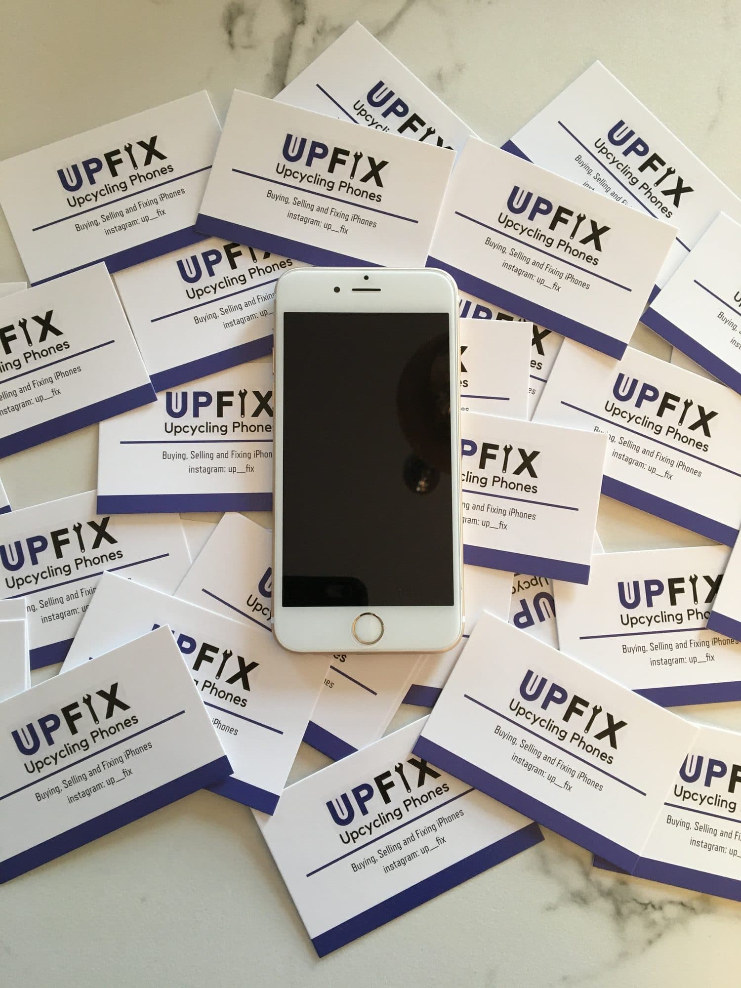 A refurbished iPhone resting on a scattered pile of UpFix business cards.